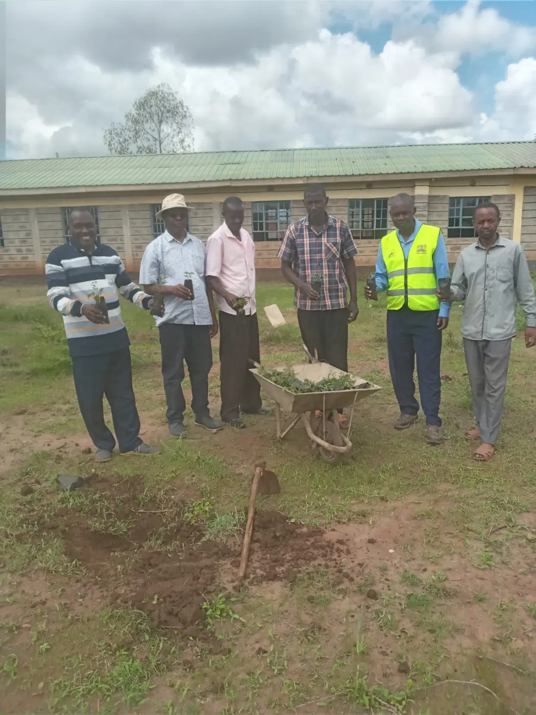 Alumni and school representatives gather around a newly planted tree.
